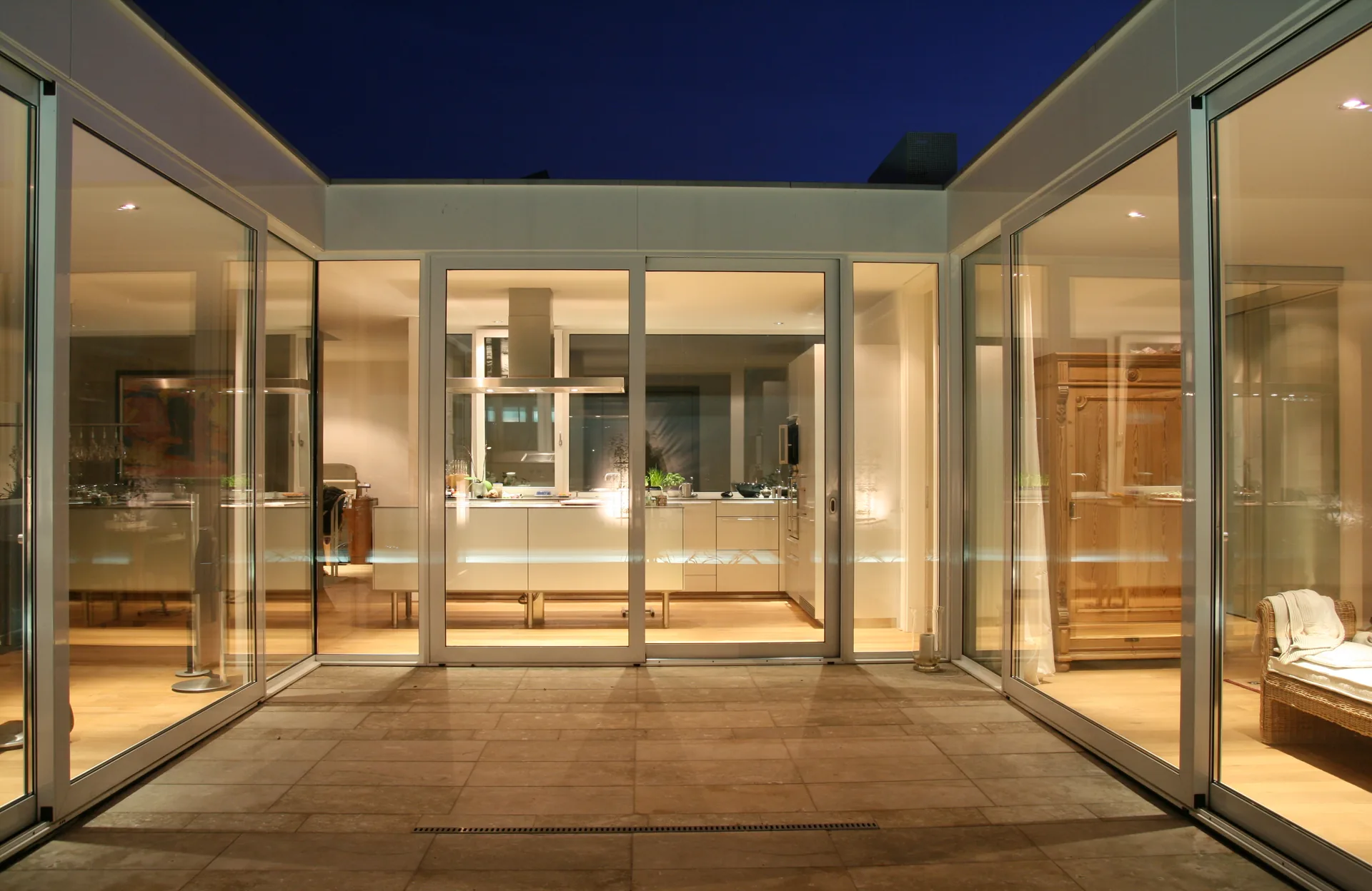 Poolhaus am Abend mit verglastem Innenhof und großen Glasfronten.