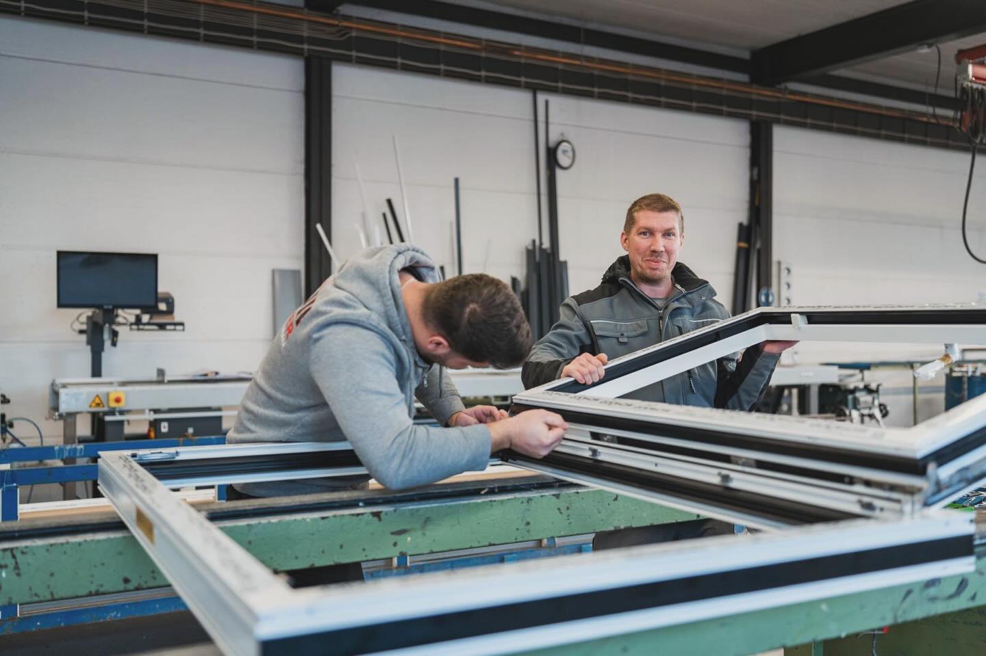 Zwei Mitarbeiter bauen in der Werkstatt einen Fensterrahmen aus Aluminium.