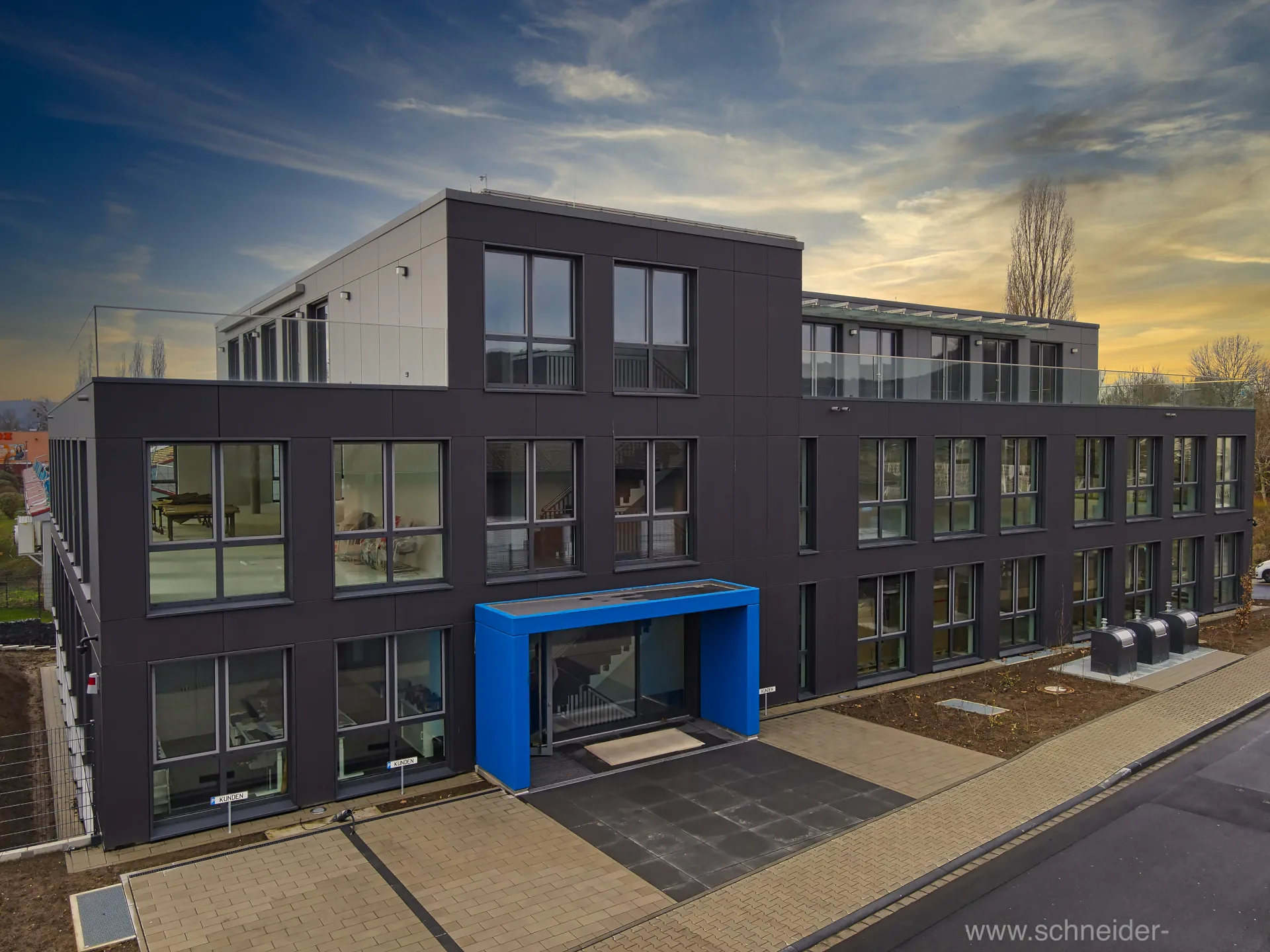 Bürogebäude mit anthrazitfarbener Fassade und blau abgesetztem Eingang.