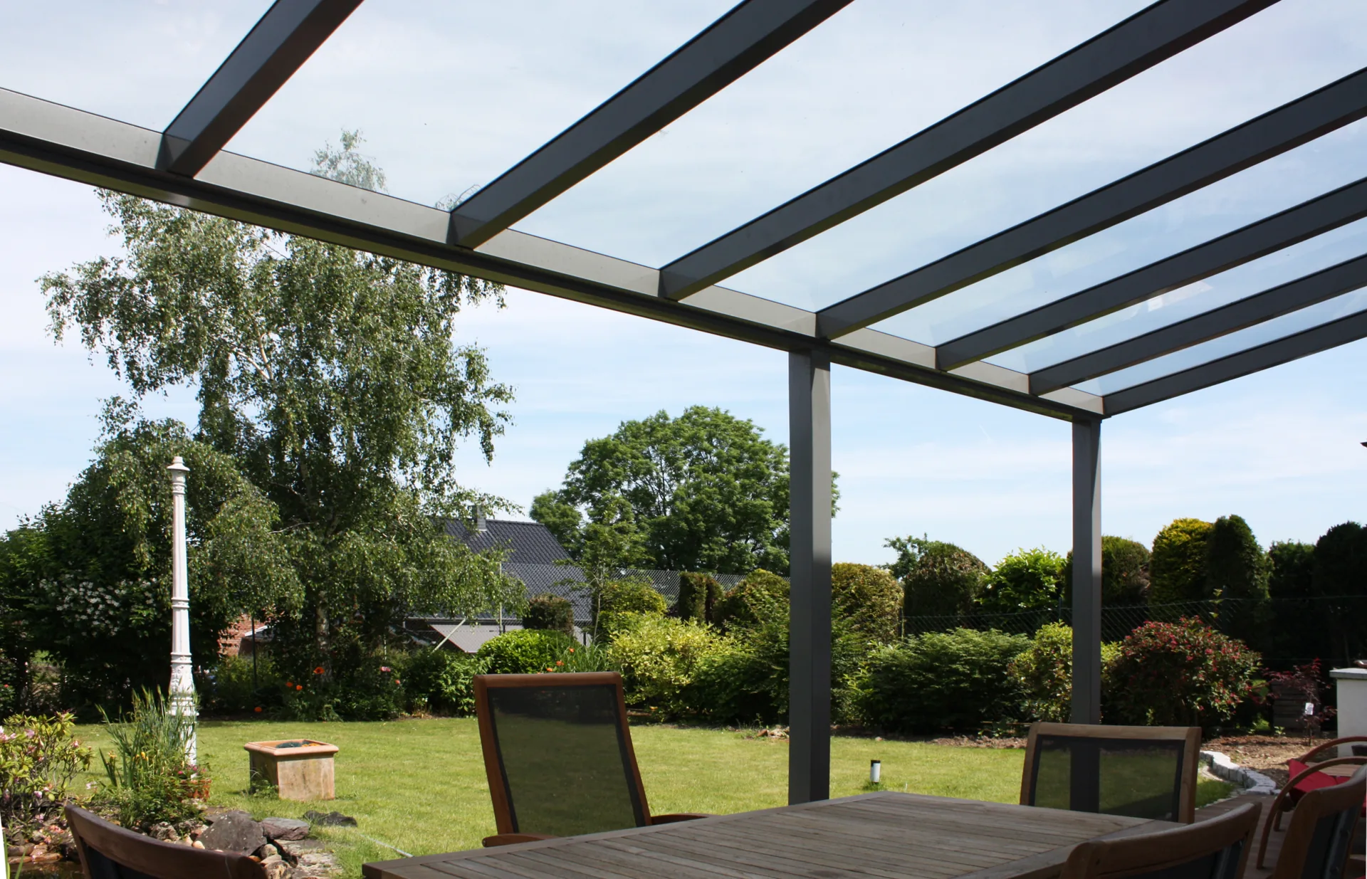 Glas-Terrassendach mit anthrazitfarbenen Profilen im Garten.